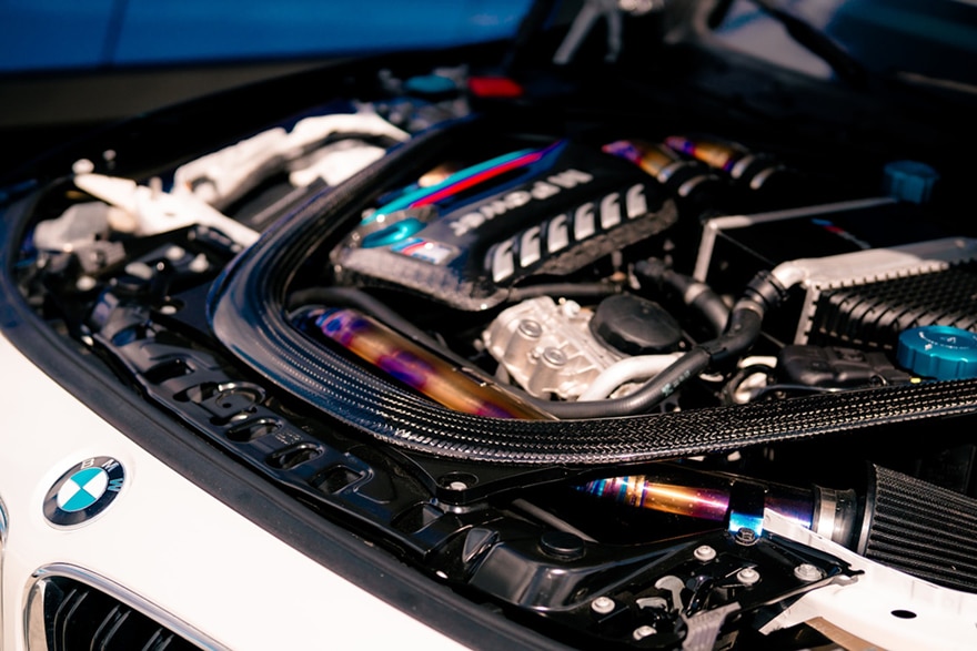 Close-up of a BMW engine featuring carbon fibre detailing, titanium components, and the iconic BMW logo on the hood.